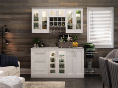 a white cabinet with wine glasses and bottles on it in a room that has wood paneling