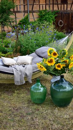 a hammock with sunflowers and two green vases on the ground