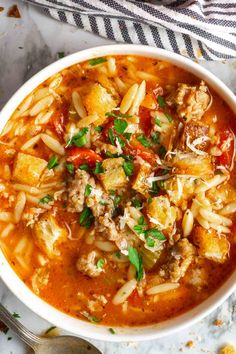 a white bowl filled with pasta and meat soup on top of a marble countertop