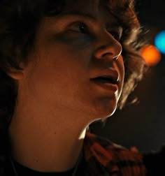 a close up of a person wearing a necklace and looking off into the distance with blurry lights in the background