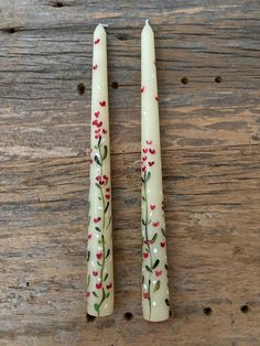 two candles sitting on top of a wooden table next to each other with flowers painted on them