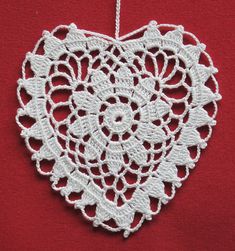 a white crocheted heart hanging on a red background