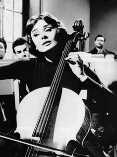 an old black and white photo of a woman holding a cello in front of other people