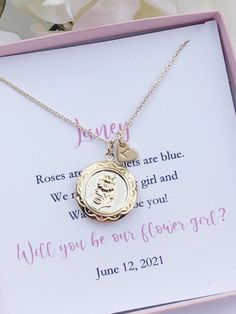 a gold necklace with a photo on it in a pink box next to white flowers