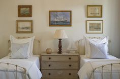 two twin beds with white linens in a bedroom next to paintings on the wall