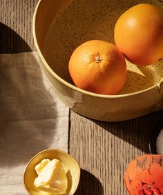 two oranges are sitting in a bowl next to some other fruit on a table