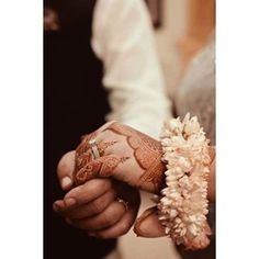 the bride and groom are holding hands with henna tattoos on their arms, both wearing wedding rings