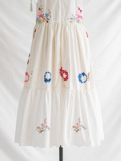 Embrace eco-chic elegance with our Floral Harmony Midi Dress. Crafted from sustainable upcycled cotton, it features a square neckline, adjustable tie straps, and exquisite cross-stitch floral embroidery adorning a pristine white base. Colorful floral wreaths add a touch of whimsy and floral embroidered tiered flared hemline with lace detailing completes the look. Care: Cool machine wash. Dry at a lower heat and press with a medium iron.  Condition: Embrace the distinctive charm of this upcycled treasure, where imperfections are unique features. Delight in the occasional loose thread or subtle discoloration, each adding to the character and history of this special garment. Floral Wreaths, Eco Chic, Gifts For New Mums, Unique Features, Pearl Jewellery Earrings, Dress Medium, June Birth Stone, Independent Designers Fashion, Jacket Sale