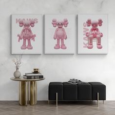 two pink teddy bears sitting on top of a table next to a black ottoman in front of a white wall