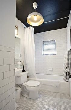 a white toilet sitting next to a bath tub in a bathroom under a light fixture