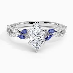 an oval shaped diamond and blue sapphire engagement ring with leaves on the band, set in 18k white gold