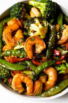 a white bowl filled with shrimp, broccoli and green beans on top of a table