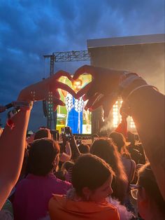 people are holding up their hands in the shape of a heart at an outdoor concert