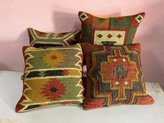 three decorative pillows sitting on top of a white table in front of a pink wall