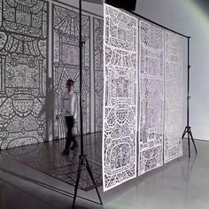 a woman is standing in front of a white screen with intricate designs on it,