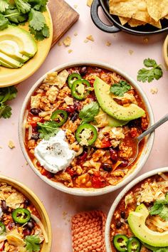 three bowls filled with chili, beans and tortilla chips on a pink surface