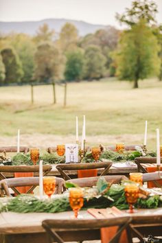 an outdoor table set up with candles and greenery