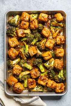 chicken and broccoli with sesame seeds in a pan on a gray table top