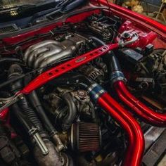 the engine compartment of a red car with its hood up and hoses running through it