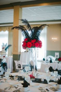 a tall vase filled with red roses and black feathers on top of a white table