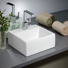 a white square sink sitting on top of a counter next to towels and vases