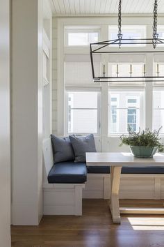 a white table with blue cushions and a bench in front of it, next to a window