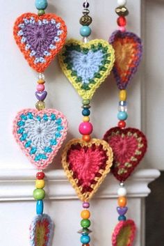 multicolored crocheted hearts hanging from a white wall with beaded beads