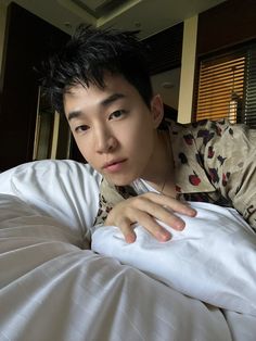 a young man laying on top of a bed next to a white comforter and pillows