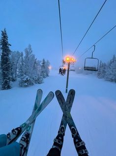 two skiers are seen from the bottom of a ski lift in the snow at dusk