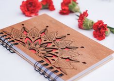 a wooden notebook with an intricate design on the cover and red carnations in the background