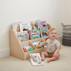 a baby sitting on the floor in front of a bookshelf filled with children's books