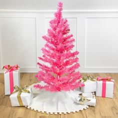 a pink christmas tree surrounded by presents on the floor with white walls and wooden floors