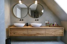 two round mirrors on the wall above sinks in a bathroom with wooden cabinets and drawers