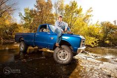 a man sitting on the back of a blue pickup truck in a river with trees around