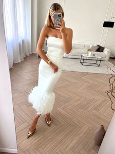 a woman in a white dress taking a selfie with her cell phone while standing on the floor