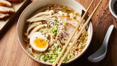 a bowl of ramen with chopsticks and an egg on the side next to some bread