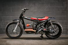 a black and red motorcycle parked in front of a brick wall with wheels on it