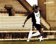 a young man kicking a soccer ball on top of a field in front of an empty bleachers