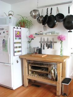 a kitchen with pots and pans hanging on the wall next to an island in front of a refrigerator