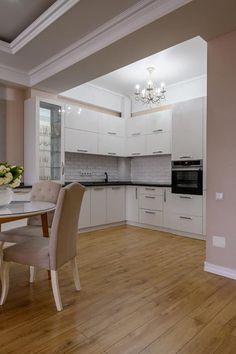 a dining room table and chairs in a kitchen with white cabinets, wood floors and a chandelier hanging from the ceiling