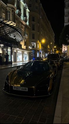 a row of parked cars on the side of a street next to tall buildings at night