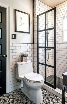 a white toilet sitting in a bathroom next to a walk in shower and black door