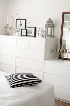 a bedroom with white furniture and black and white pillows on the bed in front of a large mirror