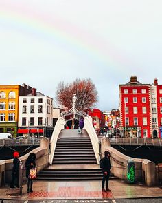 people are walking up and down the stairs in front of some buildings with a rainbow in the sky