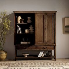 a wooden cabinet with books and vases on it's shelves next to a rug