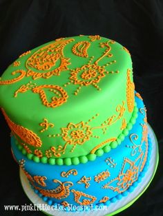 a three layer cake decorated with green, blue and orange icing on a black background