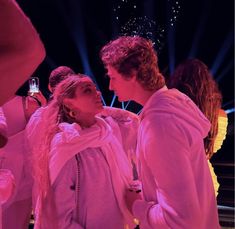 two people standing next to each other in front of a stage with bright lights and confetti on their heads