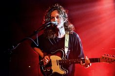 a man with long hair playing guitar on stage