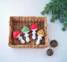 three crocheted mushrooms sitting in a basket next to pine cones