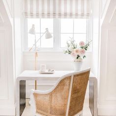 a white desk and chair in front of a window with flowers on the table next to it